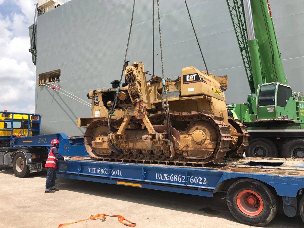 CAT crawler tractor craned onto a low-bed trailer alongside a geared vessel