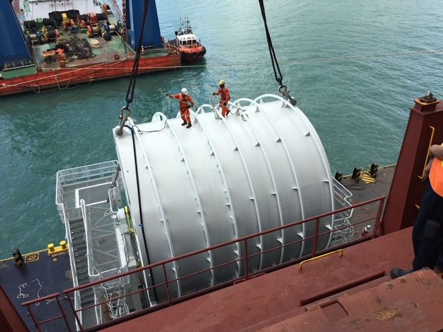 Steel cargo module strapped on a barge deck alongside port cranes